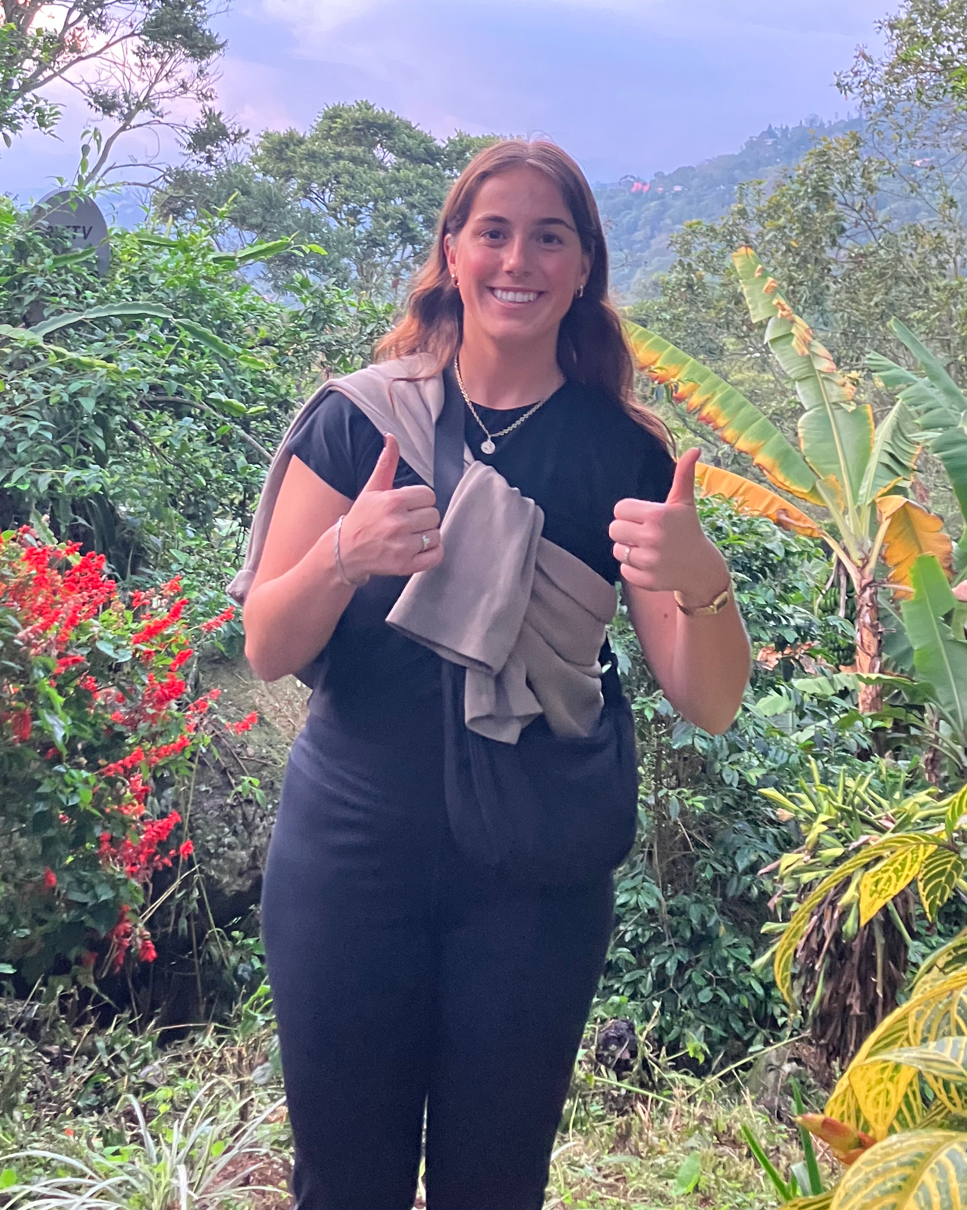 Student poses with thumbs up with a Colombia forest in the background