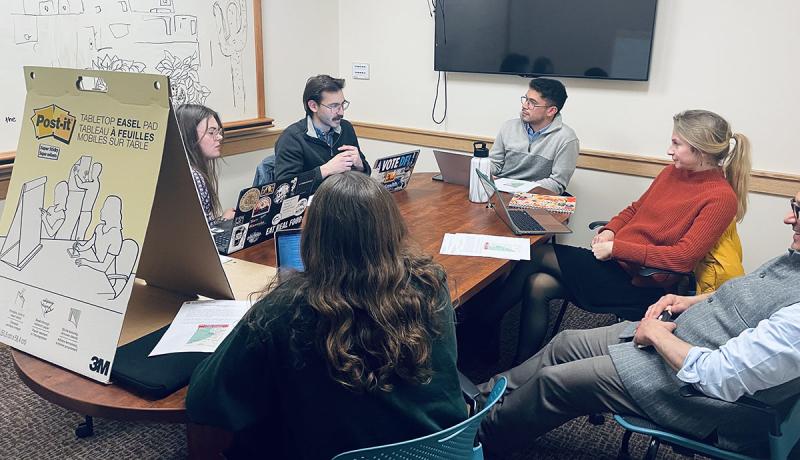 Students sit around a table in a small room, engaged in discussion.