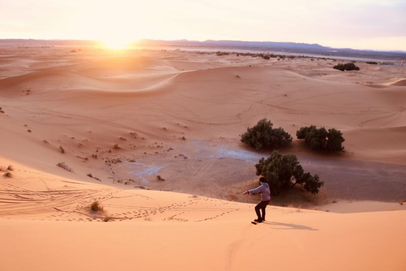 Photo by Rayna Rosenthal of a person looking out over an expanse of sand dunes at sunset.