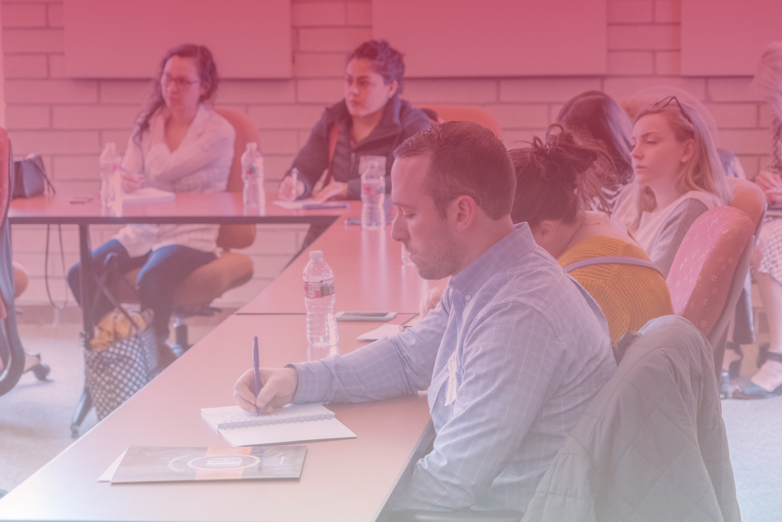 Students participating in a lecture with the student in the foreground writing in a notebook.