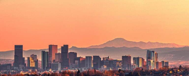 Sunset photo of the Denver skyline with the mountain range behind.