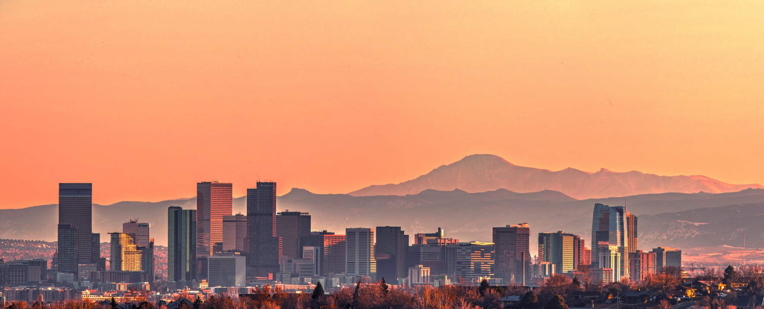 Sunset photo of the Denver skyline with the mountain range behind.