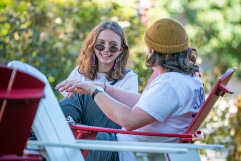 Two students talking on lawn chairs outside.