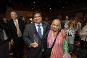 Professor Sachin Desai stands in a crowd with a family member holding his award.