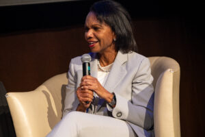 Former Secretary of State Dr. Condoleezza Rice sits in a chair and speaks into her microphone.